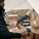 young-refugee-man-holding-box-while-volunteer-putt-2021-10-20-03-17-47-utc.webp